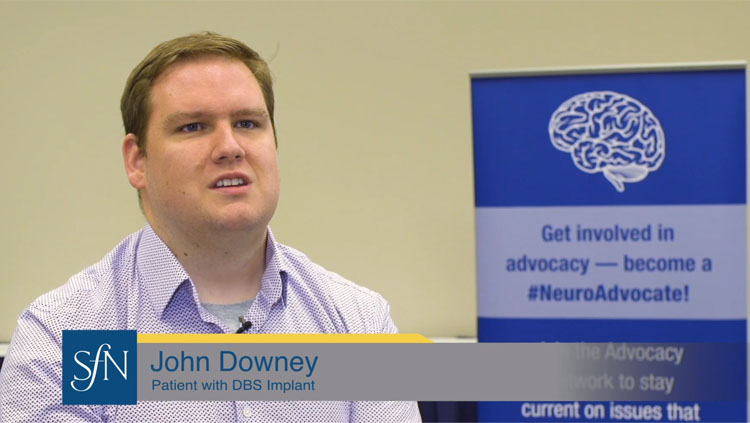 Image of John Downey wearing a lavender button down shirt speaking to the camera about deep brain stimulation.