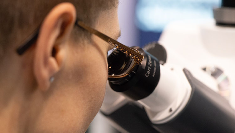 A close up of a person wearing glasses looking into a microscope.