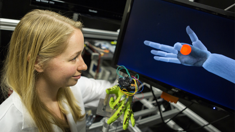 PhD student Karen Schroeder demonstrates a task in monkeys, in which they control animated finger movements with bend sensors on their fingers. Photo credit: College of Engineering, University of Michigan.