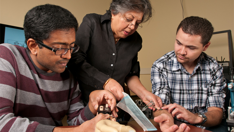 Jung discussing with Sathyakumar Kuntaegowdanahalli (left, research engineer) and Andres Pena (right, doctoral graduate student) the functioning of components of the ANS-Neural-Enabled Prosthetic Hand system: myoelectric control by the user of the prosthetic hand, and electronics for processing information from force and hand opening sensors embedded in the prosthetic hand. Courtesy of the Adaptive Neural Systems Laboratory, Florida International University.