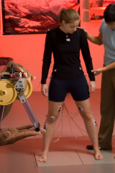 A small biomimetic robot, designed to test understanding of how the nervous system controls balance while a former PhD student in the Neuromechanics Lab, Stacie Chvatal, stands on two force plates. She is instrumented with electrodes on the skin.