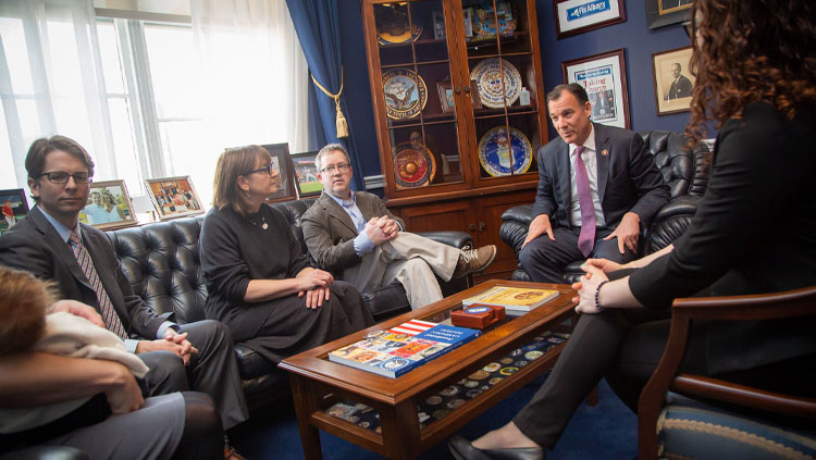 six people sit around a wood table having a conversation.