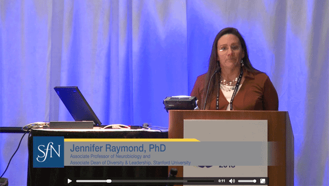 Jennifer Raymond stands at a podium and talks to neuroscientists about how challenges in the field can bring change.