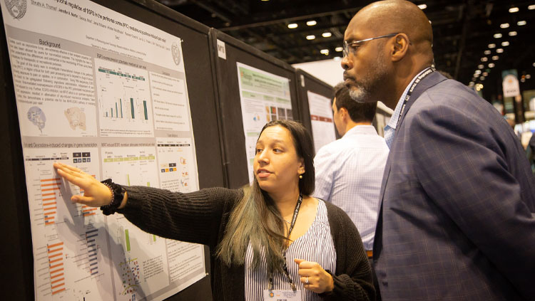 Image of a young woman explaining her poster presentation to a man at Neuroscience 2019.