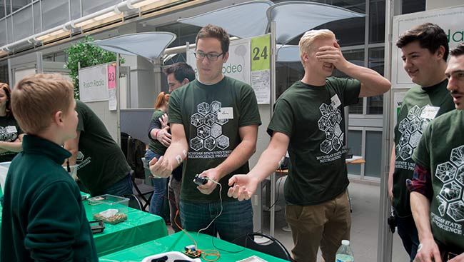 Male neuroscientists interact with children at an outreach event. 