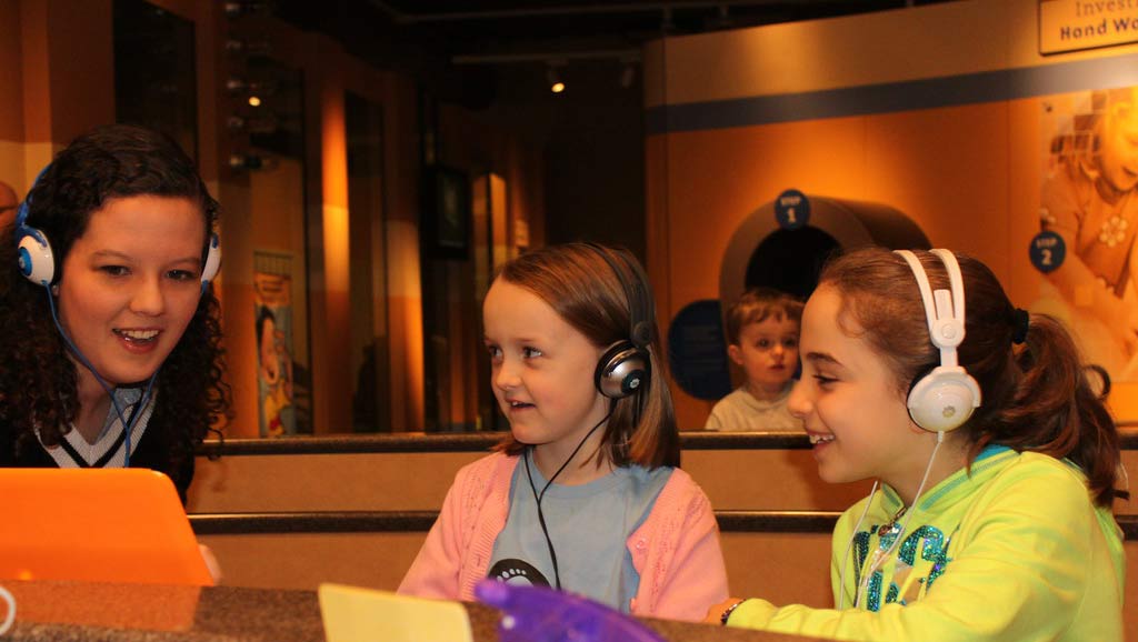 Two children participate in a science activity with a female neuroscientist.