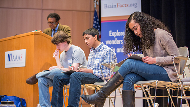 Three students sit on a stage to participate in a presentation