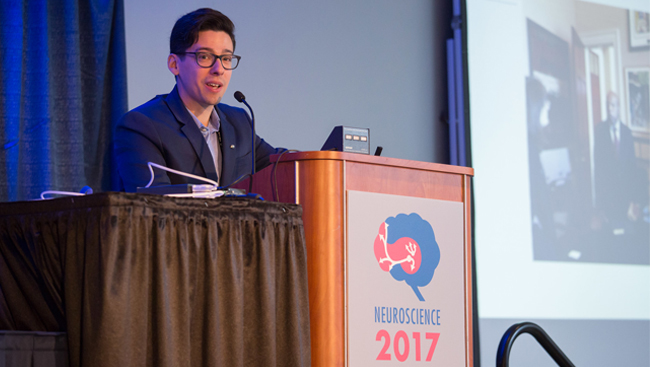 Michael Wells gives a speech standing at a podium at Neuroscience 2017.
