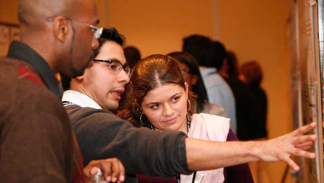 A male presents his scientific research poster to others.