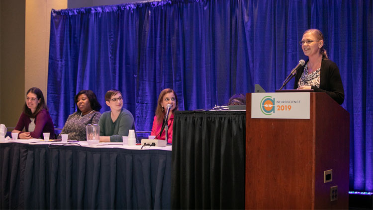 Four women panelists sit listening intently to a speaker.