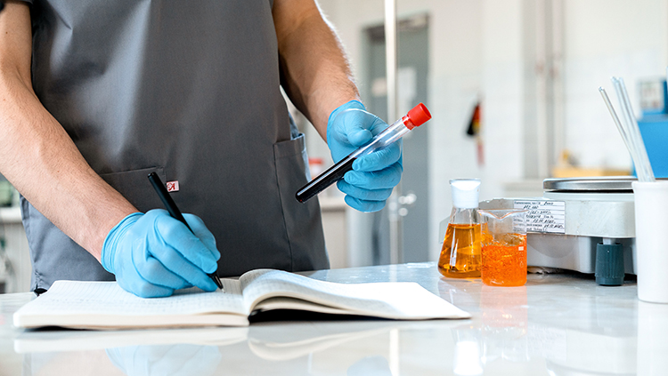 Researcher recording data while holding test tubes.