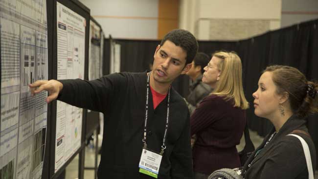 A poster presenter explaining his research to an annual meeting attendee