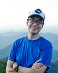Headshot of David Brann wearing a blue shirt and a hat with mountains in the background.