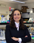 Image of Christie Fowler standing in a lab with her arms crossed wearing a black jacket.