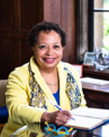 Image of Joanne Berger-Sweeney sitting at a desk in a yellow jacket.