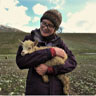 Image of Lara Rogerson-Wood standing in a field holding a goat.